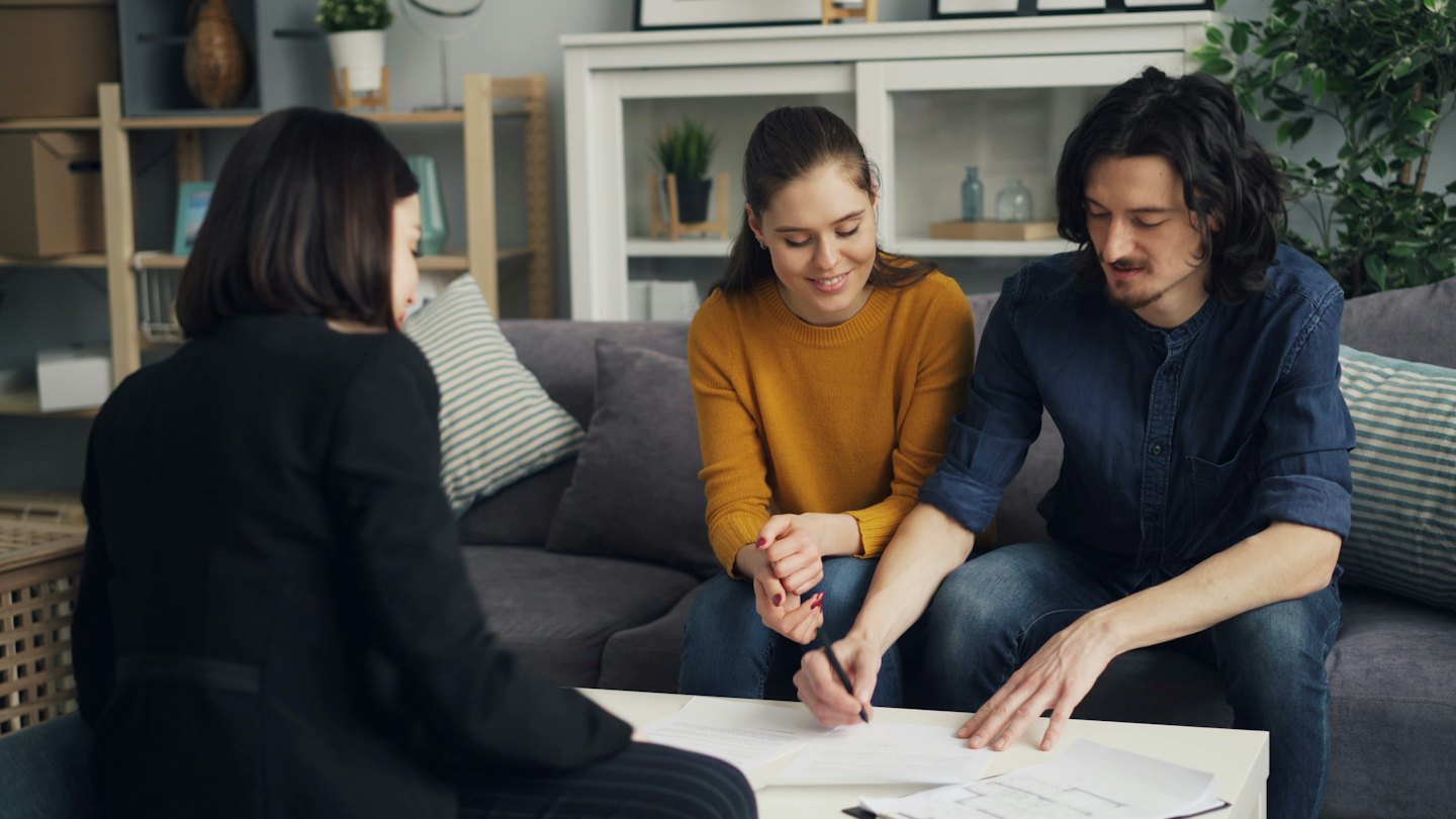 Couple signs documents with a professional in a living room.